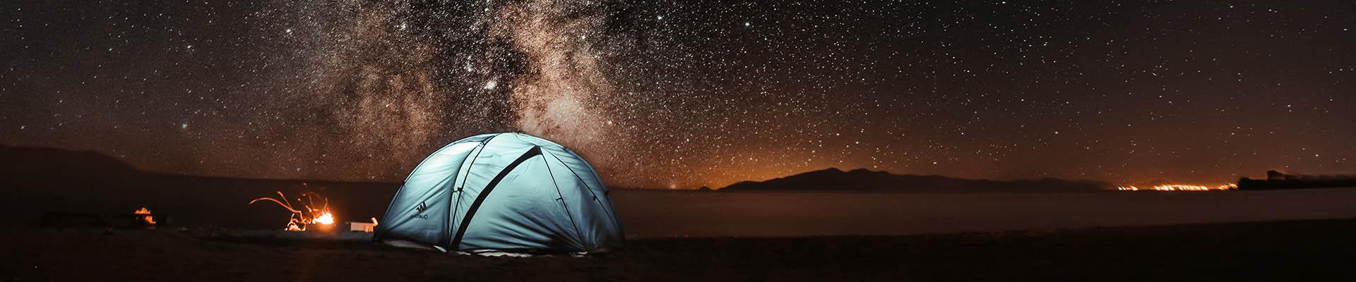 A blue tent out it the desert under a starry nigh